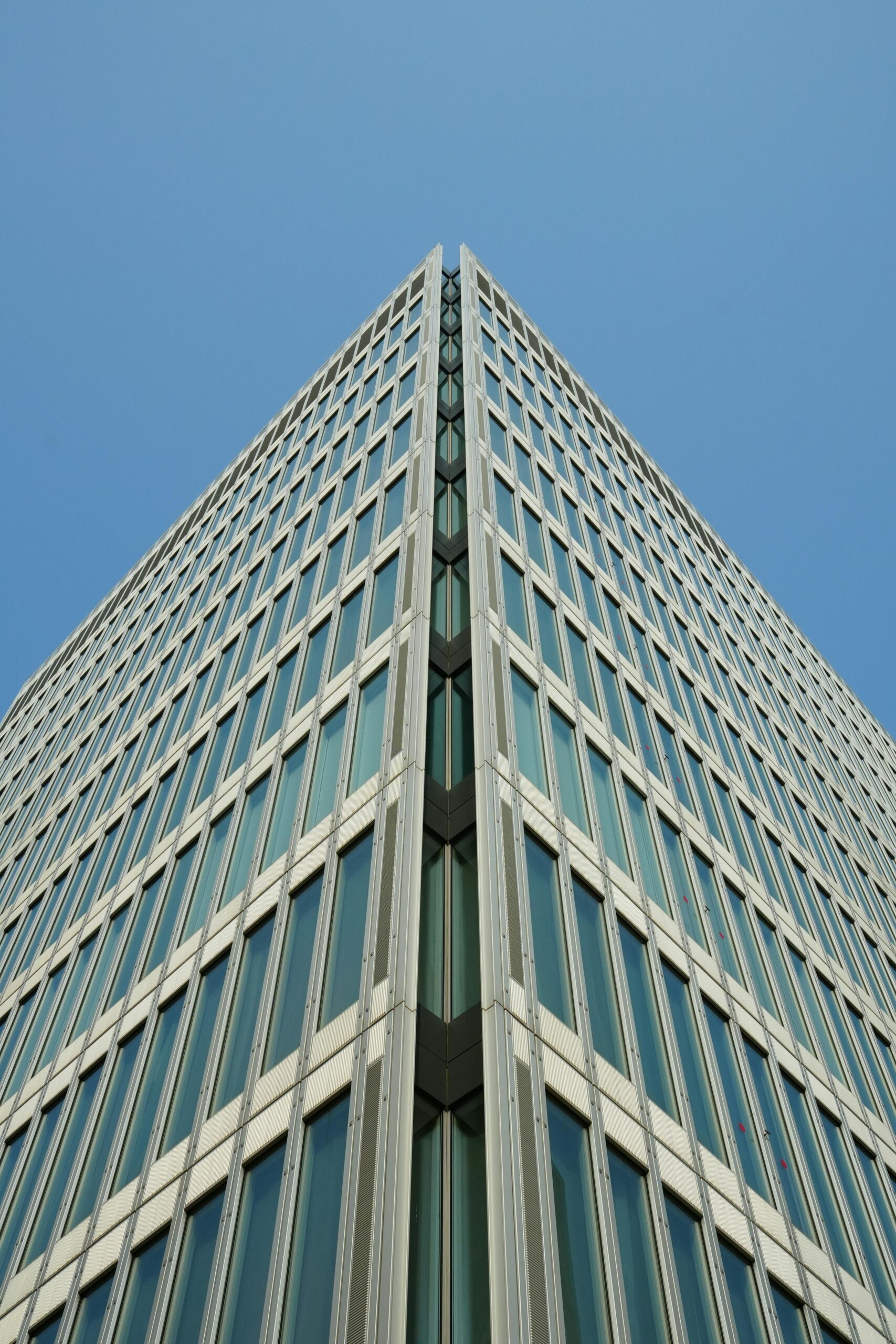 Stunning architectural shot of a contemporary glass skyscraper meeting a clear blue sky, showcasing modern design elements.